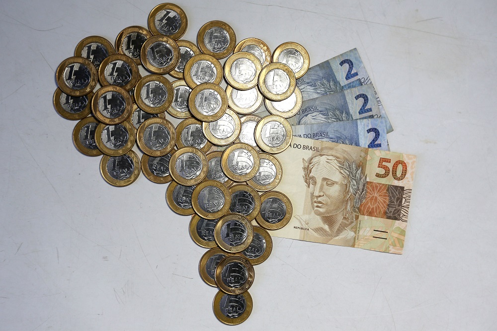 Pessoa analisando investimentos com gráficos, notas de real e destaque para 13,75% representando Selic alta