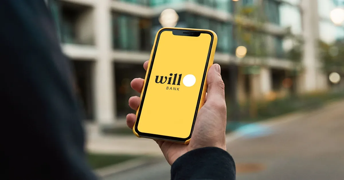 Smartphone exibindo aviso de liquidação do Will Bank com prédio institucional desfocado ao fundo