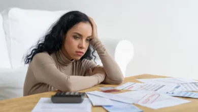 Cliente na agência bancária solicitando cartão de crédito, atendente ao fundo e smartphone com app do banco em primeiro plano
